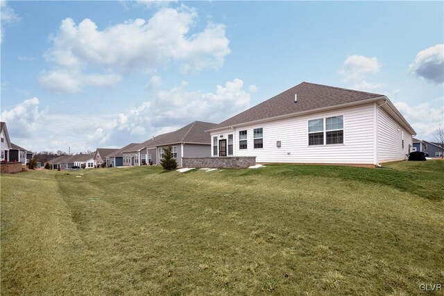 rear view of property featuring roof with shingles, a residential view, and a yard