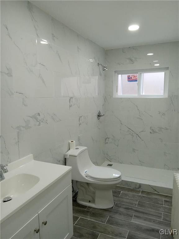 bathroom featuring tile walls, vanity, tiled shower, and toilet