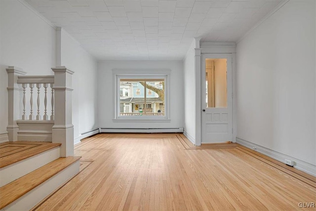 unfurnished living room featuring light wood-style floors, stairs, a baseboard heating unit, and crown molding