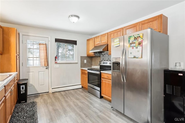 kitchen with appliances with stainless steel finishes, tasteful backsplash, baseboard heating, light hardwood / wood-style floors, and sink