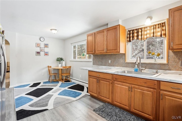 kitchen featuring sink, a baseboard radiator, decorative backsplash, and light hardwood / wood-style flooring