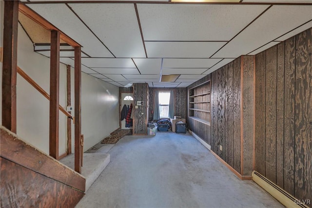 basement featuring built in shelves, a baseboard heating unit, and wood walls