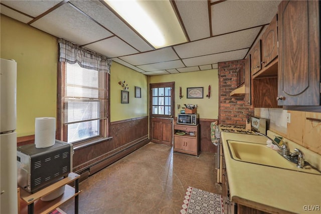 kitchen with wood walls, white refrigerator, sink, a paneled ceiling, and a baseboard radiator