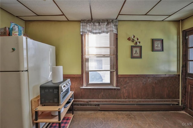 kitchen with a paneled ceiling, a baseboard radiator, white refrigerator, and wooden walls