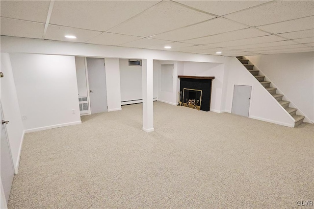 basement with a paneled ceiling, carpet floors, and a baseboard radiator