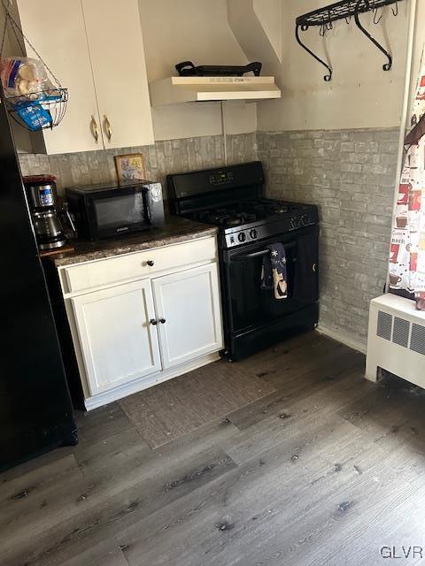 kitchen featuring white cabinets, dark countertops, radiator, dark wood-style floors, and black appliances