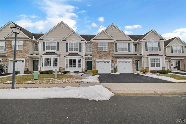 townhome / multi-family property with a garage, driveway, and stone siding