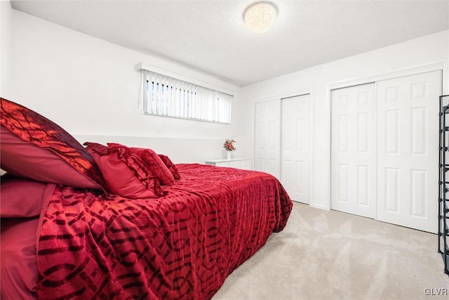 bedroom featuring light carpet, a textured ceiling, and multiple closets