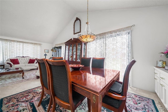 dining area with vaulted ceiling and light colored carpet