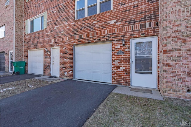 doorway to property with driveway, brick siding, and an attached garage