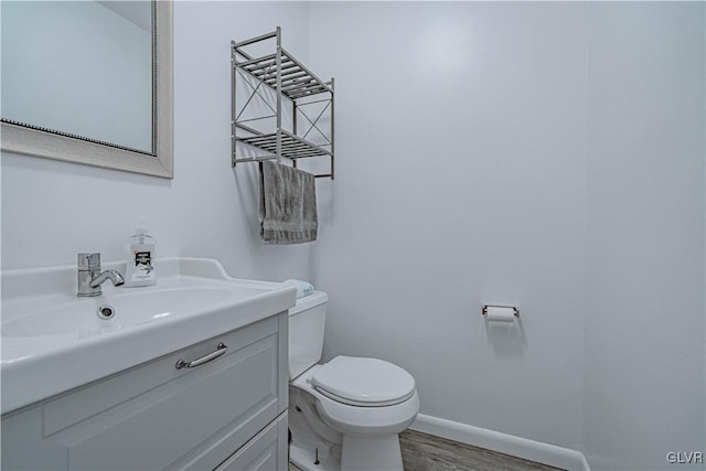 half bath featuring toilet, baseboards, wood finished floors, and vanity