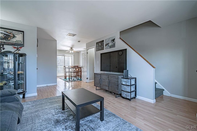 living room featuring baseboards, visible vents, stairway, and light wood finished floors