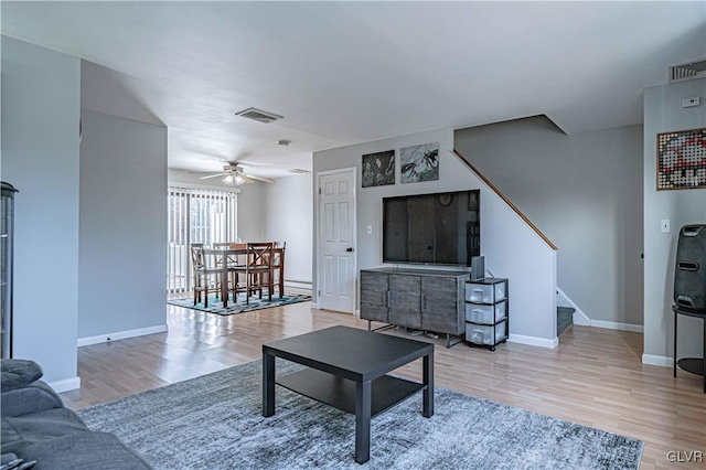 living room featuring light wood-style floors, visible vents, stairway, and baseboards