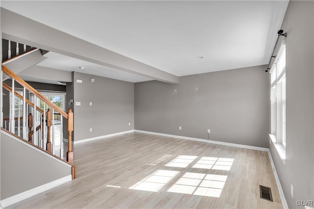 unfurnished room featuring light wood-style floors, visible vents, baseboards, and stairs