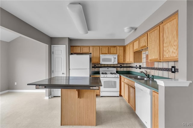 kitchen featuring a breakfast bar area, white appliances, a kitchen island, a sink, and dark countertops