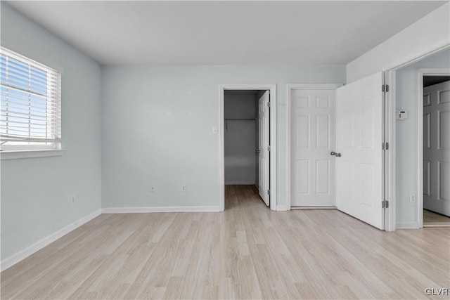 unfurnished bedroom with a closet, light wood-style flooring, baseboards, and a spacious closet