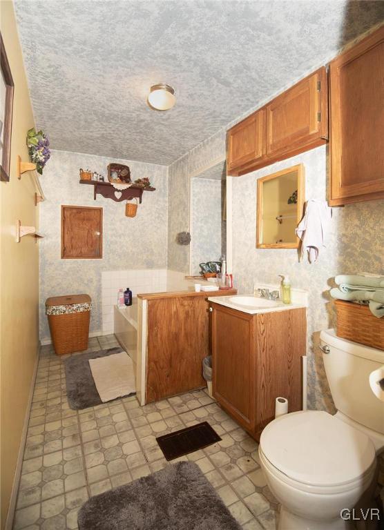 bathroom with a textured ceiling, toilet, vanity, and baseboards