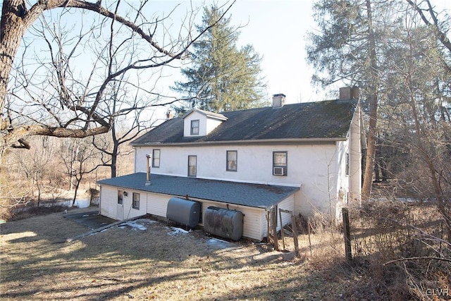 back of house with a chimney, heating fuel, and stucco siding