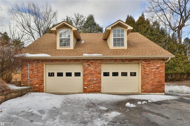 view of front of property with a shingled roof, a detached garage, and brick siding