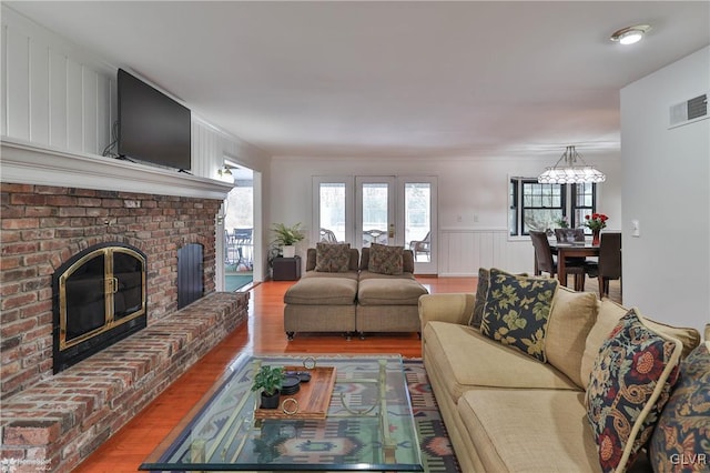 living area featuring a brick fireplace, visible vents, wood finished floors, and a wainscoted wall