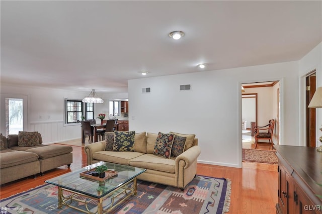 living room featuring wainscoting, visible vents, an inviting chandelier, and wood finished floors