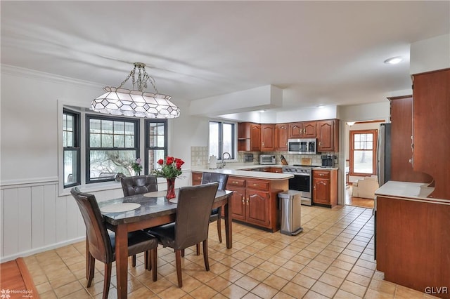 kitchen with a wainscoted wall, appliances with stainless steel finishes, hanging light fixtures, light countertops, and backsplash