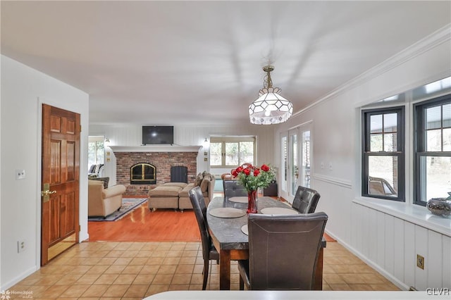 dining space featuring light tile patterned floors, ornamental molding, a wainscoted wall, and a fireplace