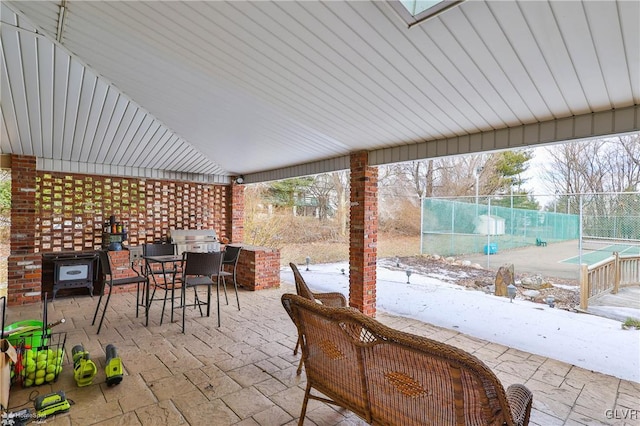 view of patio with a tennis court, outdoor dining space, an outdoor kitchen, and fence