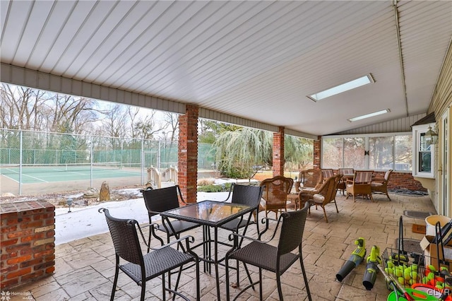 view of patio / terrace with a tennis court, outdoor dining area, and fence