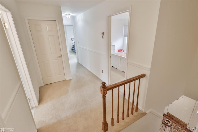 hall with light colored carpet and an upstairs landing