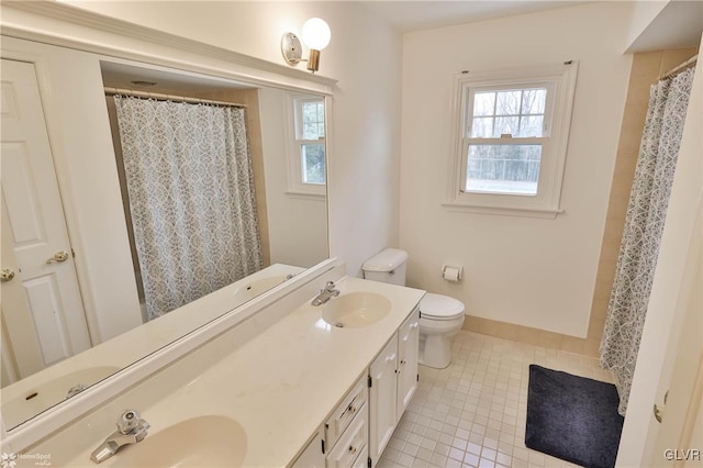 full bath with double vanity, toilet, a sink, tile patterned flooring, and baseboards