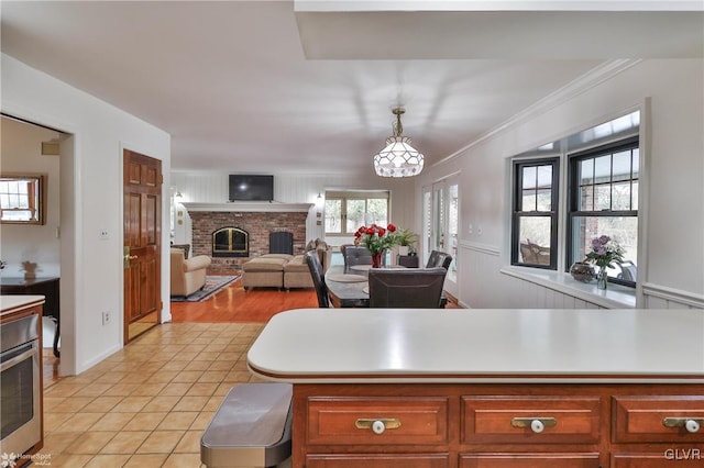 kitchen with light tile patterned floors, ornamental molding, hanging light fixtures, light countertops, and a fireplace