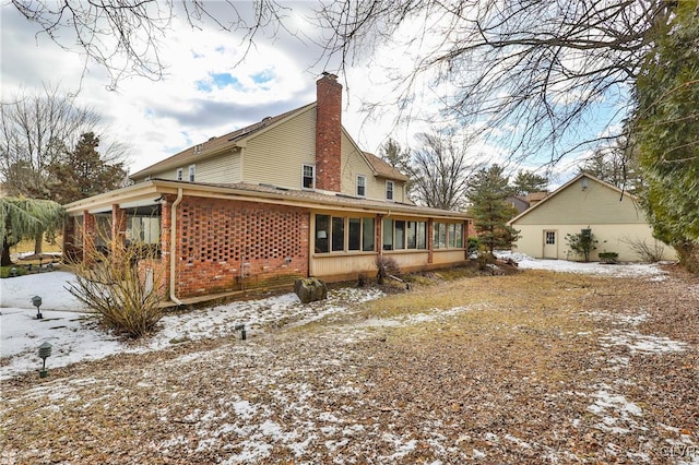 snow covered rear of property with a sunroom, brick siding, and a chimney