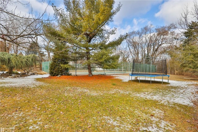 view of yard with a tennis court, a trampoline, and fence