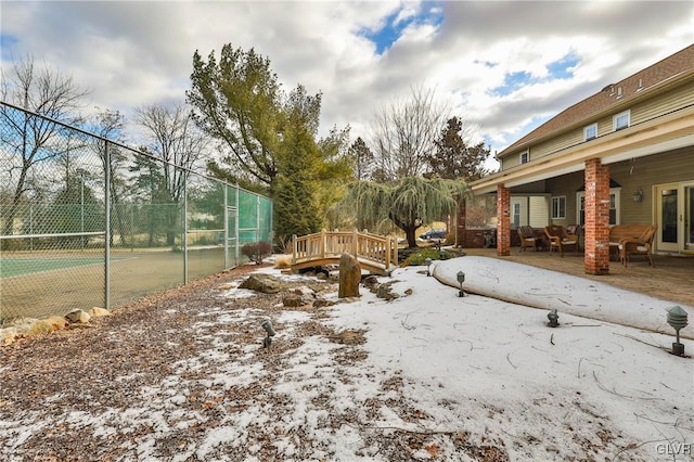 snowy yard with a tennis court, fence, and a patio