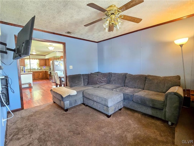 living area featuring carpet floors, ceiling fan, visible vents, and crown molding