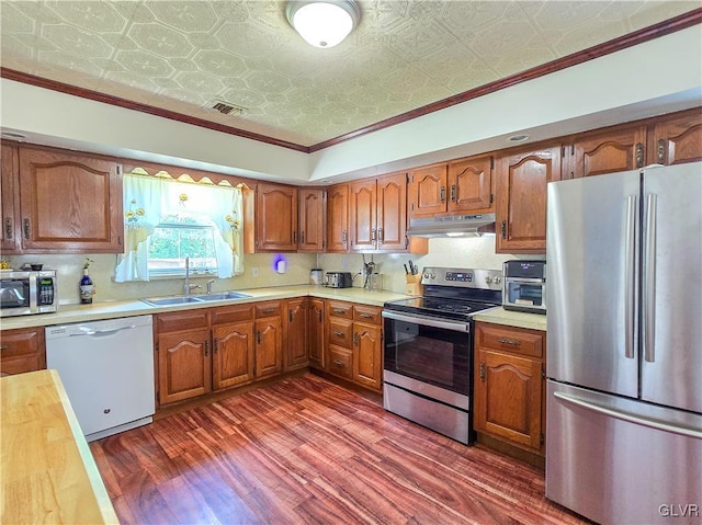 kitchen featuring under cabinet range hood, a sink, light countertops, appliances with stainless steel finishes, and an ornate ceiling