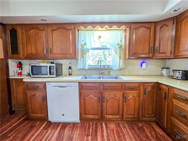 kitchen with light countertops, stainless steel microwave, brown cabinetry, white dishwasher, and a sink