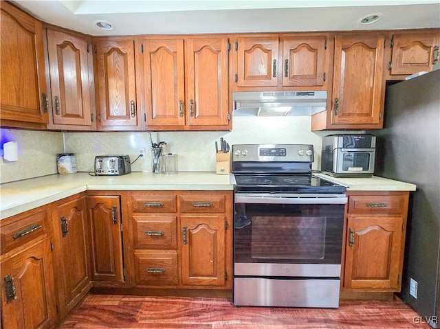 kitchen featuring under cabinet range hood, electric range, light countertops, and brown cabinetry