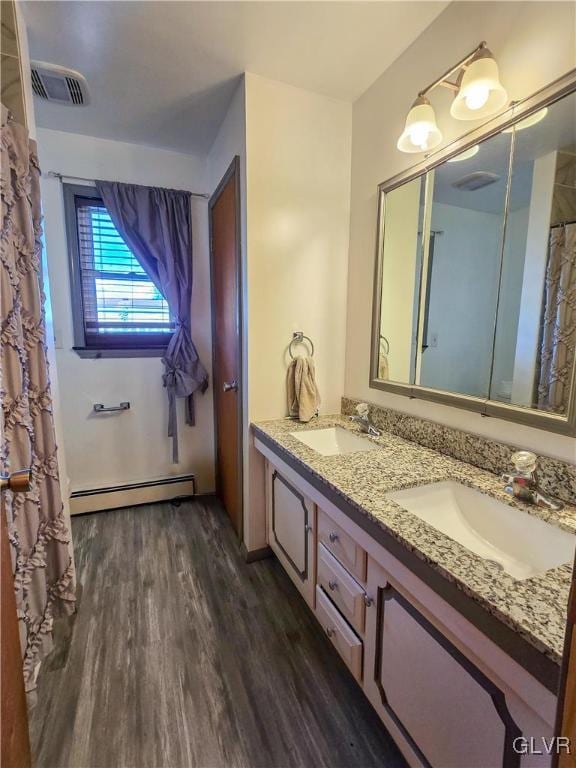 bathroom with double vanity, baseboard heating, a sink, and wood finished floors