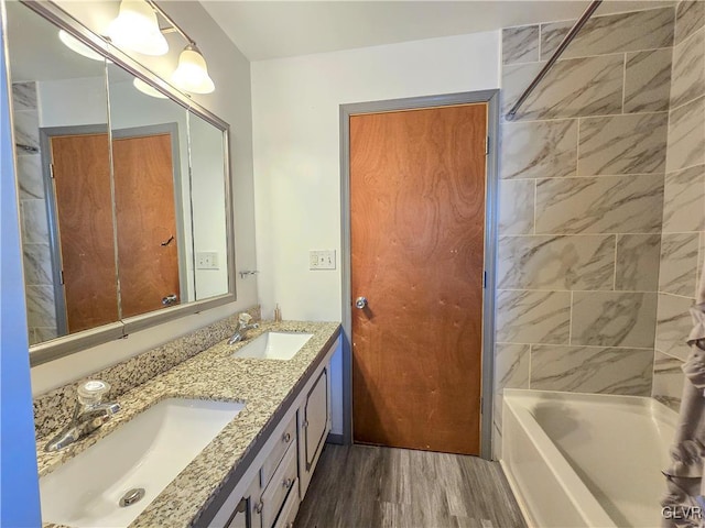 bathroom with double vanity, washtub / shower combination, a sink, and wood finished floors