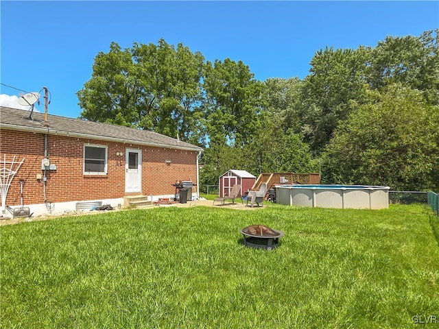 view of yard featuring entry steps, a storage shed, an outdoor fire pit, an outdoor pool, and fence