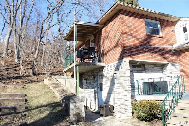 view of home's exterior with a balcony, stone siding, stairway, and brick siding