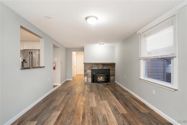 unfurnished living room featuring dark wood finished floors, a stone fireplace, and baseboards