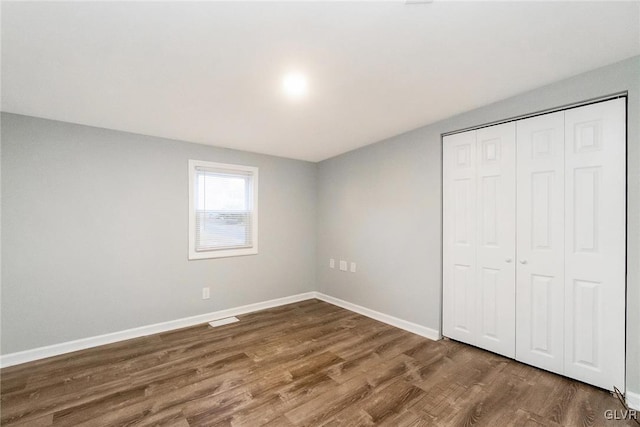 unfurnished bedroom featuring dark wood-type flooring, a closet, and baseboards