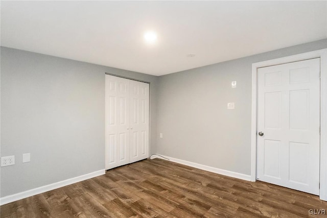 unfurnished bedroom featuring a closet, dark wood finished floors, and baseboards