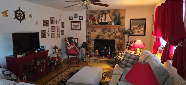 living room featuring ceiling fan, a stone fireplace, and wood finished floors