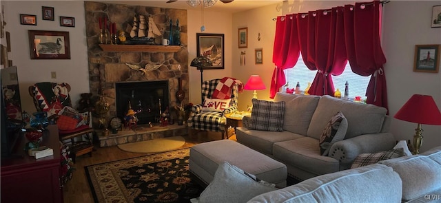 living area featuring ceiling fan, wood finished floors, and a stone fireplace