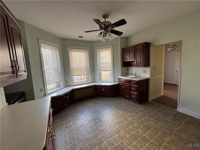 kitchen featuring baseboards, a sink, ceiling fan, light countertops, and dark brown cabinetry