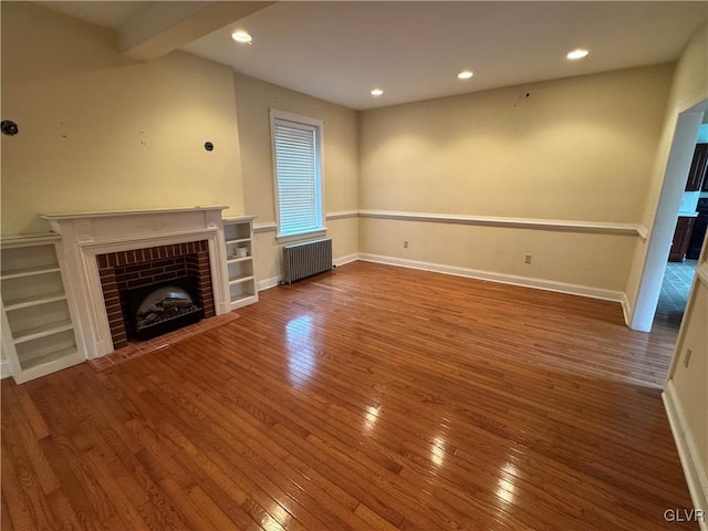 unfurnished living room with hardwood / wood-style floors, a brick fireplace, radiator heating unit, and baseboards